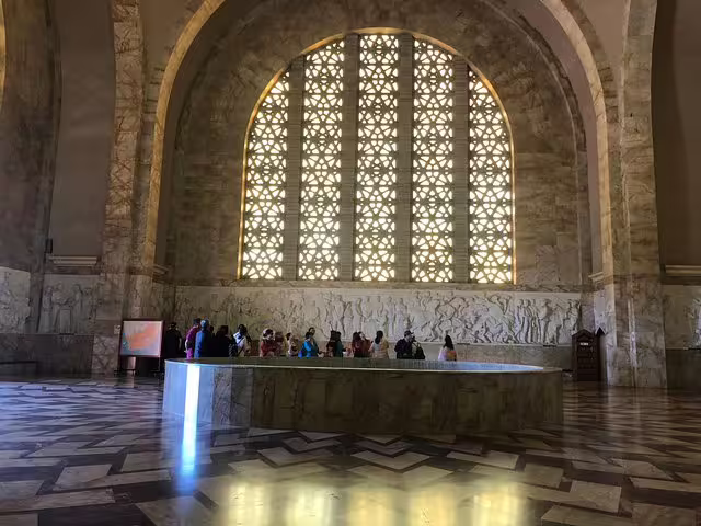 Interior view of the Voortrekker Monument with visitors, showcasing intricate window patterns and historical carvings.