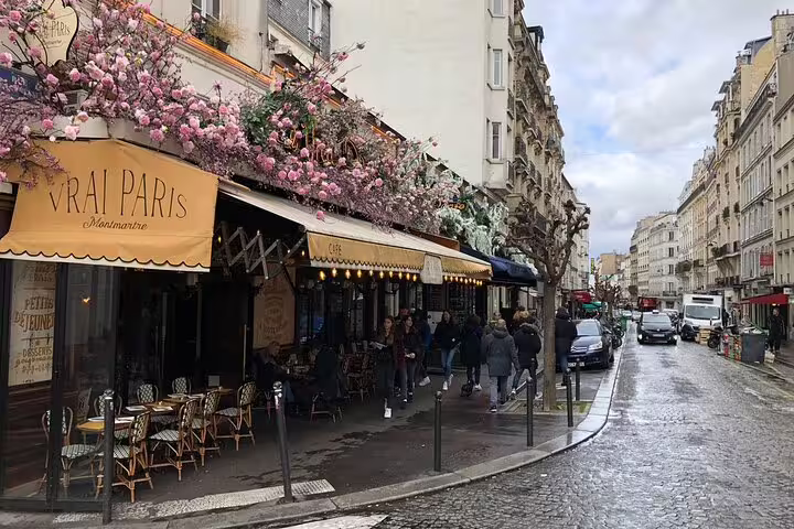 Vrai Paris café in Montmartre with pink flower decorations, yellow awning, and wet cobblestone street