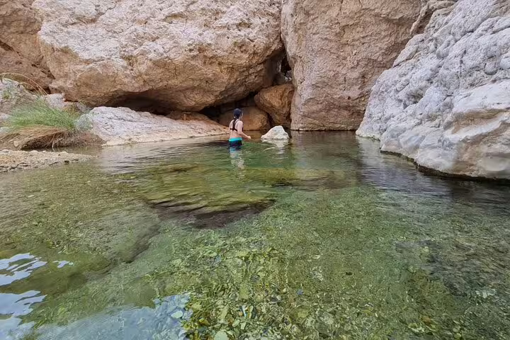 Explorer wades through the serene waters of Wadi Al Arbeieen, surrounded by rugged rock formations and clear pools.