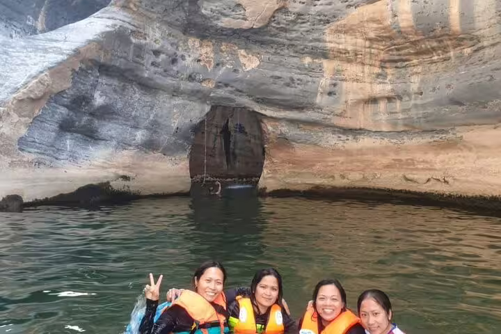 Group of tourists enjoying a swim with life vests in the scenic waters of Wadi Dham's rocky landscape.