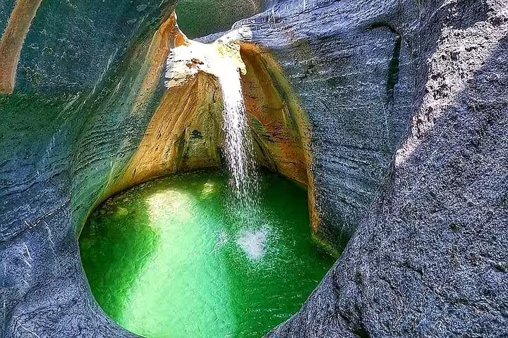 Stunning waterfall cascading into a vibrant green pool in Wadi Dham, perfect for a private full-day nature tour.
