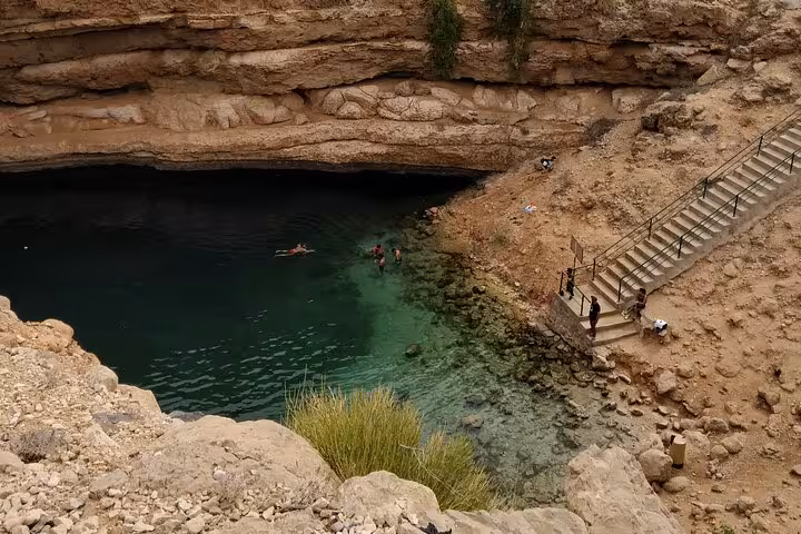 Travelers swim in the emerald waters of Bimmah Sinkhole in Oman, reached by stone steps on a Wadi Shab day trip tour
