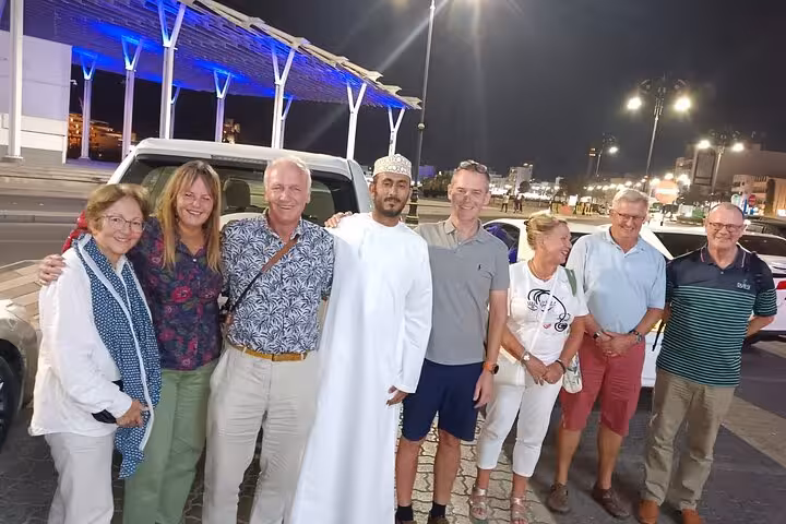 Tourists and Omani guide posing together at night in Muscat before a full-day Wadi Shab and Bimmah Sinkhole tour