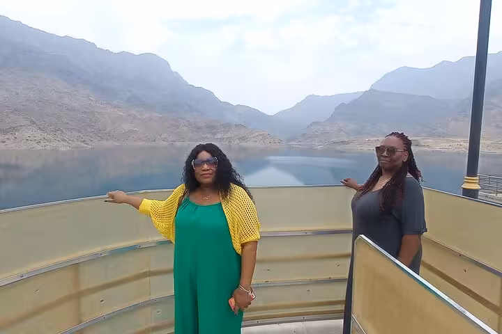 Two women posing at a scenic mountain lake viewpoint during a full-day Wadi Shab Bimmah Sinkhole tour Muscat