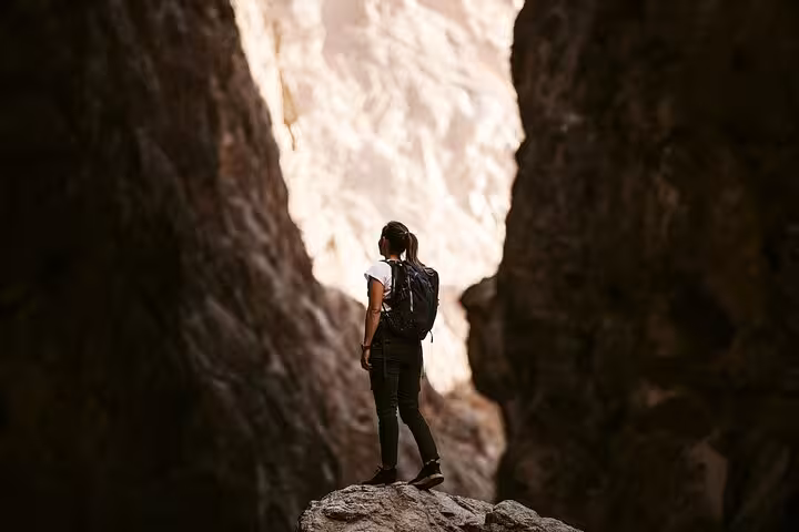 Solo hiker with backpack exploring narrow rocky canyon gorge on a Wadi Shab full-day adventure tour from Muscat