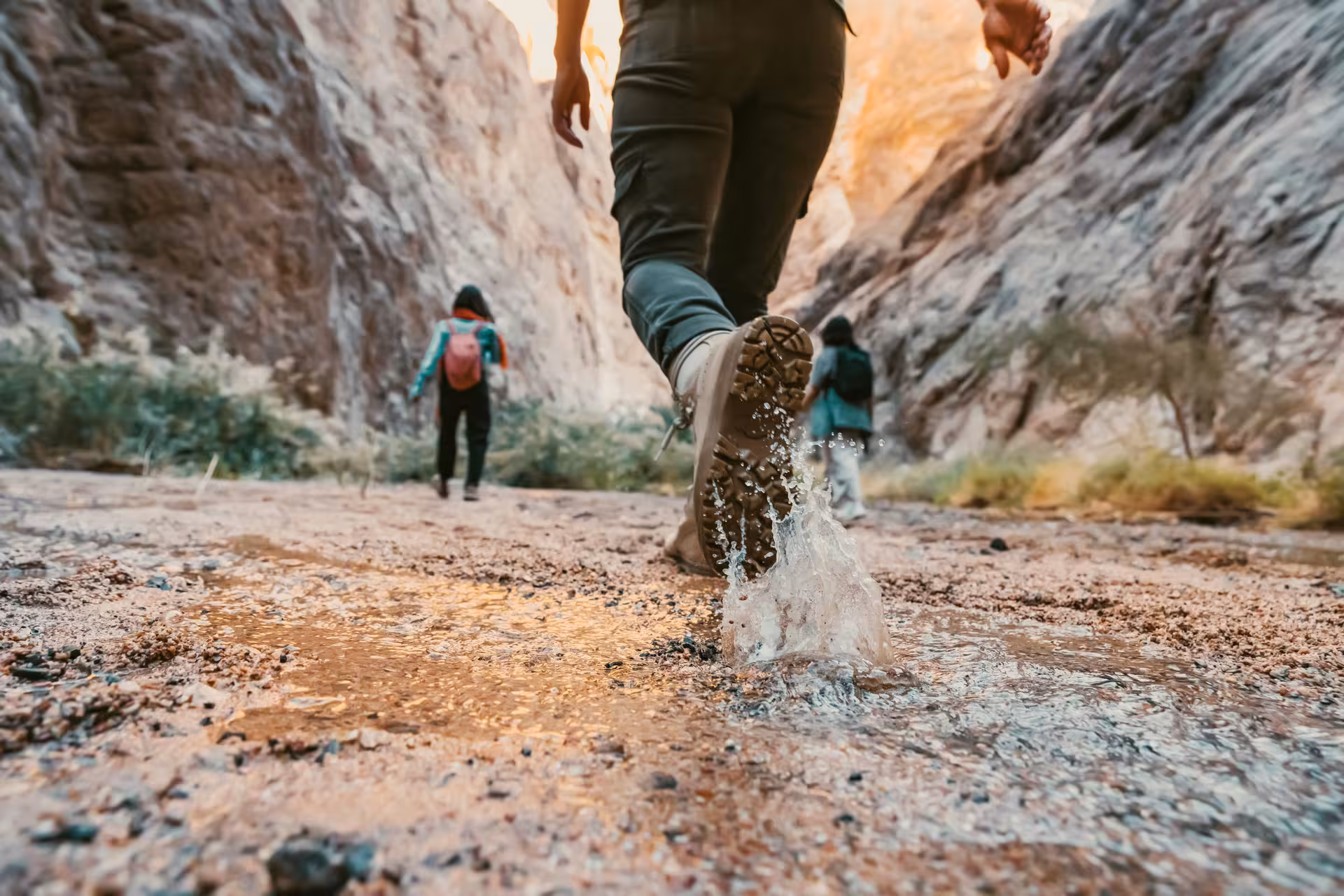 Close-up of hikers splashing through shallow water while trekking between towering cliffs in Wadi Shab, Oman