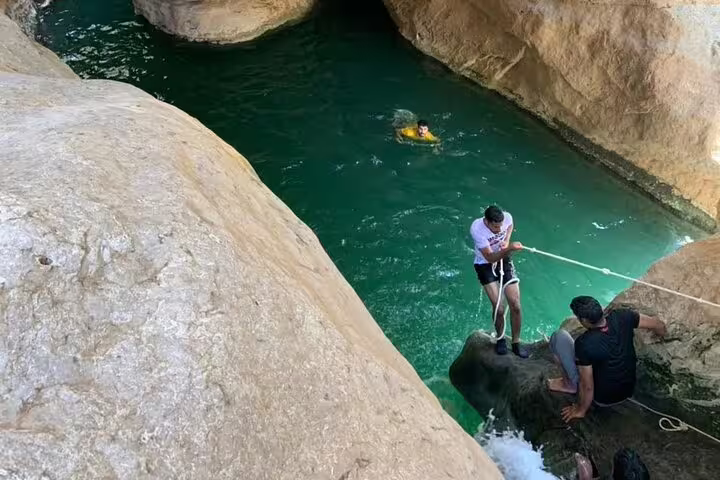 Adventure seekers enjoy rock climbing and swimming in the turquoise waters of Wadi Shab, Oman.