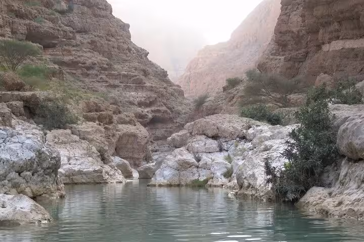Turquoise freshwater pool nestled between towering rocky canyon walls in stunning Wadi Shab Oman day tour