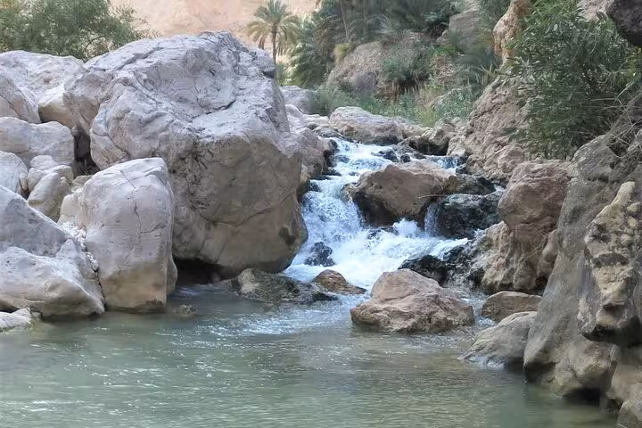 Crystal-clear turquoise waters cascade over rocks at scenic Wadi Shab Oman on a full-day tour from Muscat