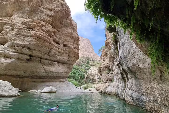 Swimmers enjoy the clear turquoise waters amidst towering rock formations at Wadi Tiwi on a full-day tour from Muscat.