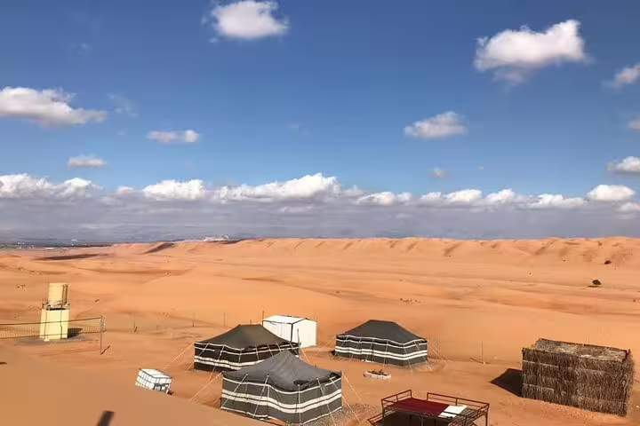 Scenic view of a desert camp in Wahiba Sands, Oman, featuring traditional tents under a blue sky with scattered clouds.