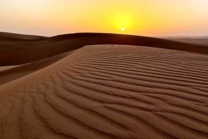 Golden sunset over the rippled sand dunes of Wahiba Sands, Oman, ideal for a 2-day private camping adventure.
