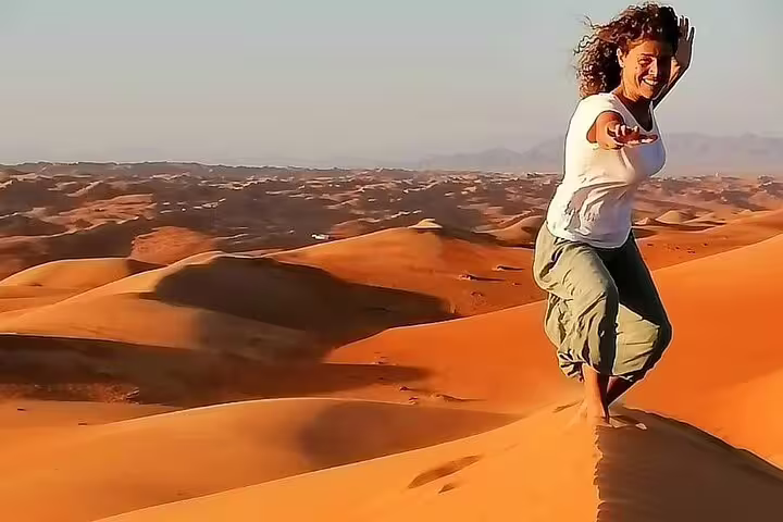 Tourist enjoying a sunny day on the golden dunes of Wahiba Sands during a private desert tour in Oman.