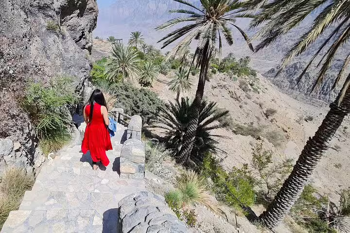Tourist in red dress exploring the rocky paths and palm trees of Wakan during the 2 Days 1 Night Wakan Private Tour.