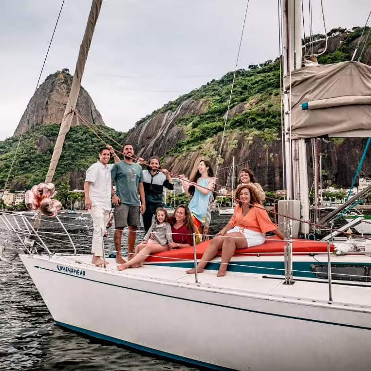 Smiling group on a sailboat with scenic mountain views, embodying the joy of Wake Up and Sail adventures.
