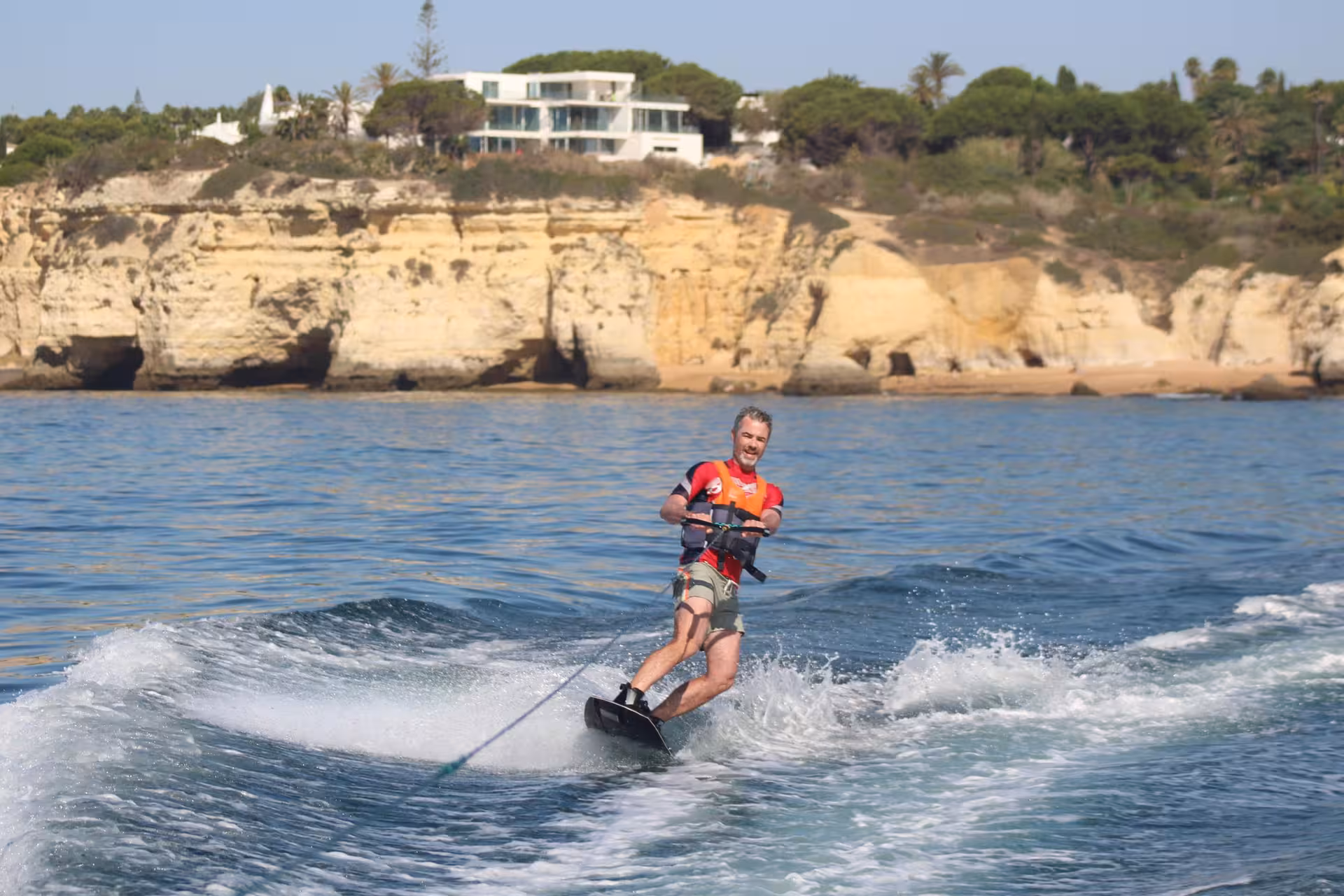 Happy man wakeboarding past golden limestone cliffs on a sunny wakeboard lesson and guided tour in Armacao de Pera