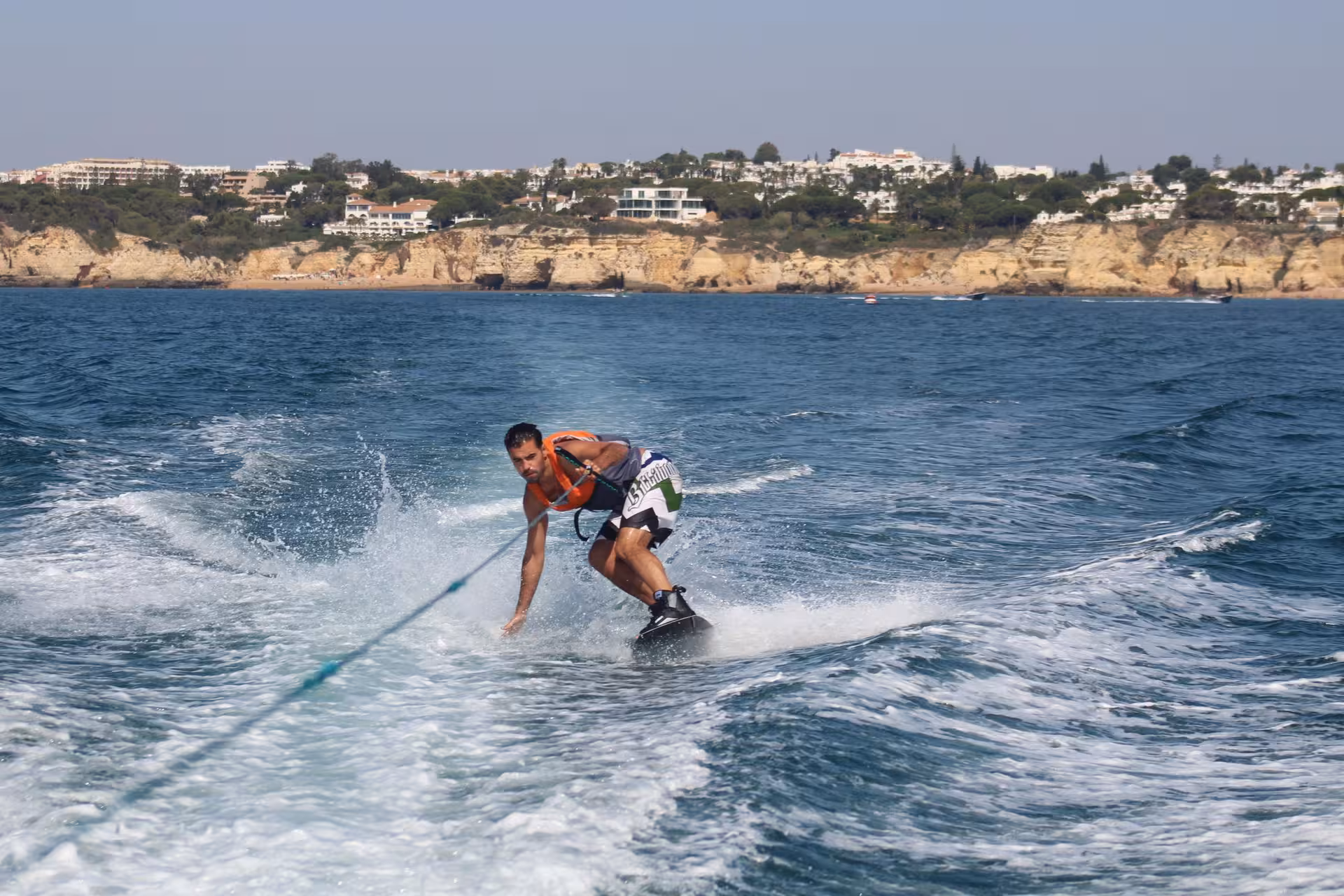 A man wakeboarding on blue waters near Armacao de Pera cliffs during a guided wakeboard lesson tour
