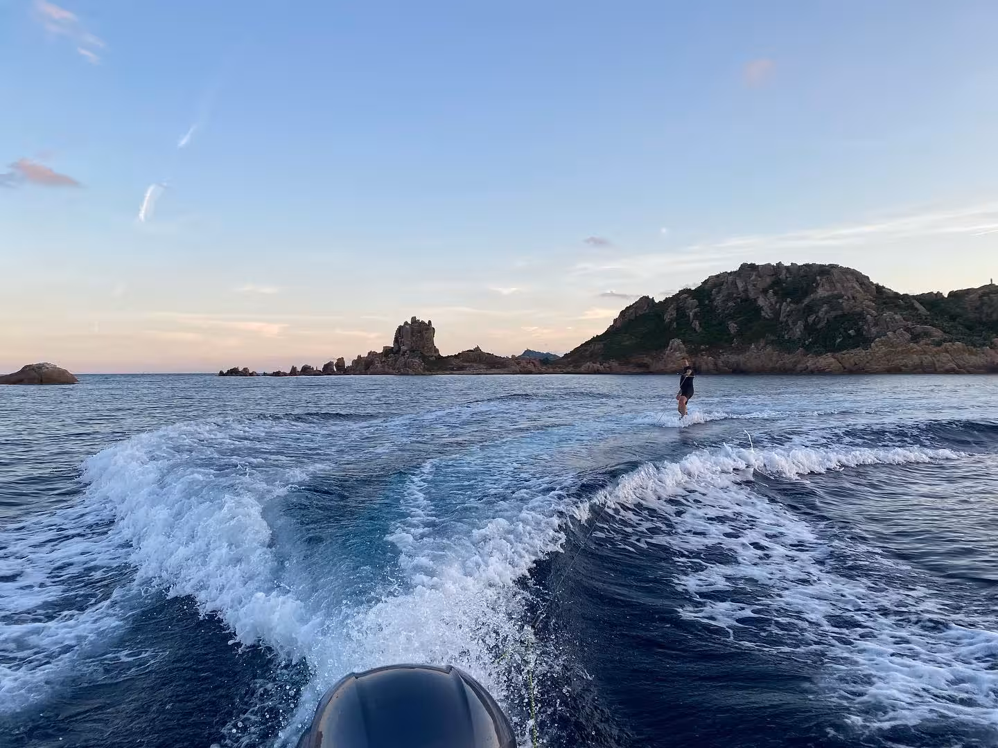 Wakeboarder riding waves in Bari Sardo at sunset, offering stunning views of Sardinia's rugged coastal landscape.