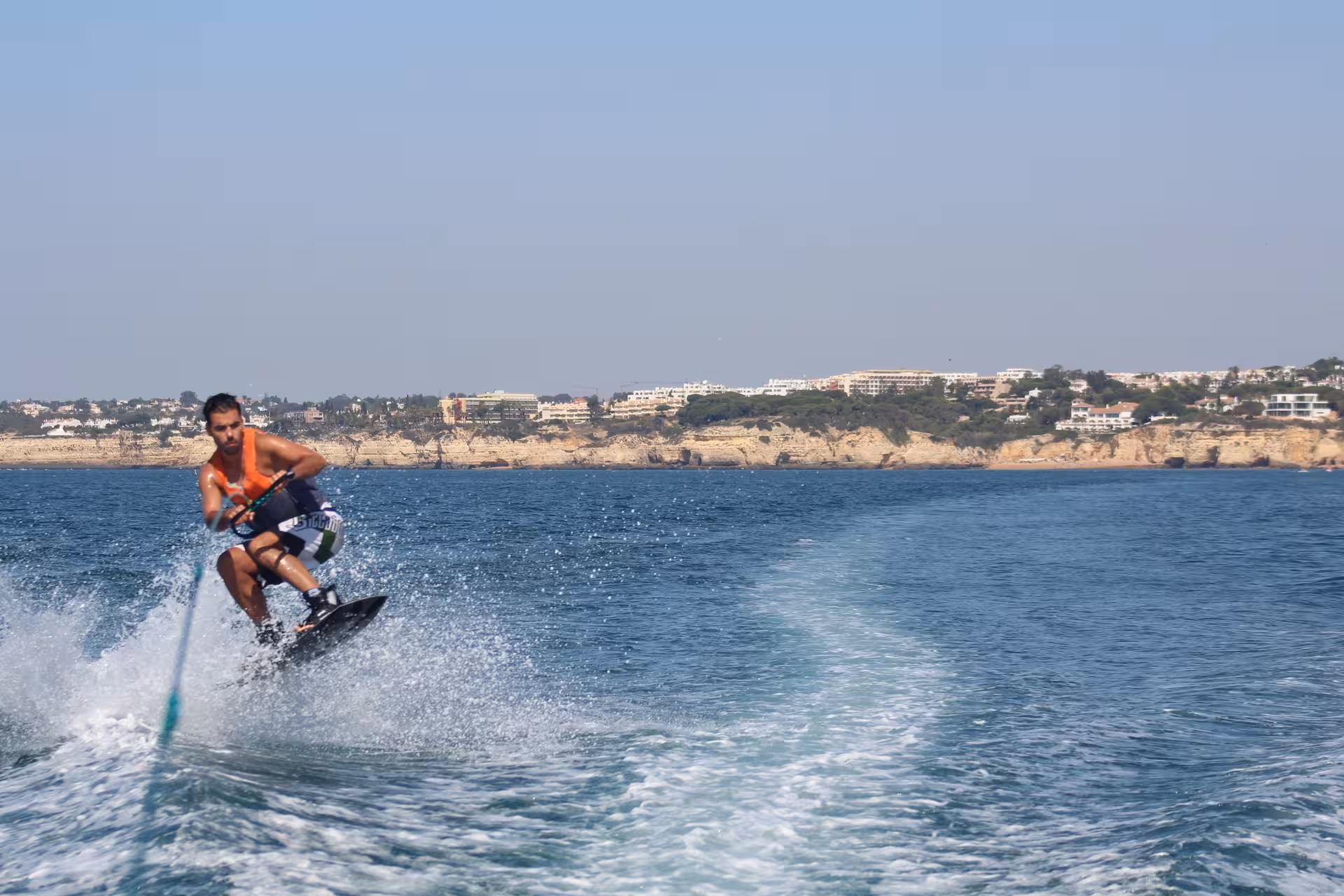 Man in orange life vest wakeboarding with speed near the scenic Algarve coastline of Armacao de Pera