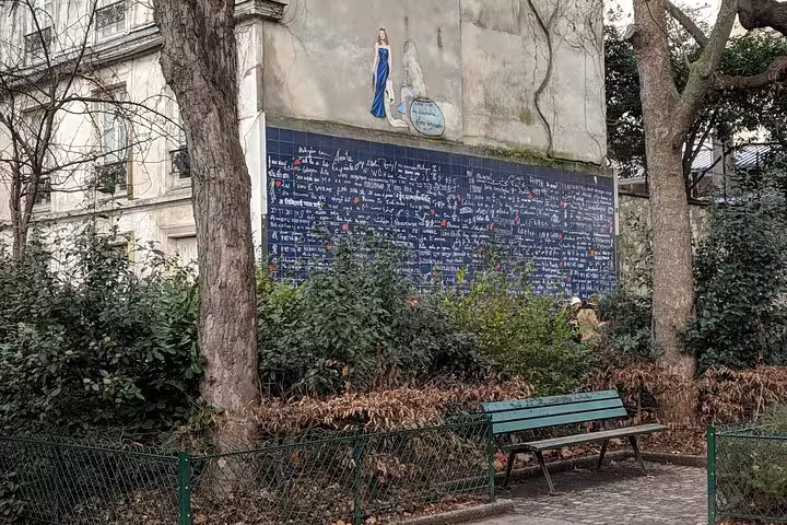Wall of Love mural covered in multilingual text in Montmartre Paris with a park bench in foreground