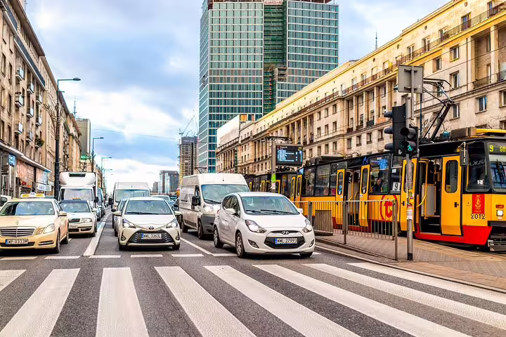 Busy Warsaw city street with yellow trams and cars at a crosswalk, modern and historic buildings in background