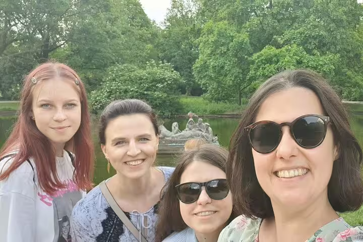 Four women smiling for a selfie in a green park with a pond and statue in Warsaw