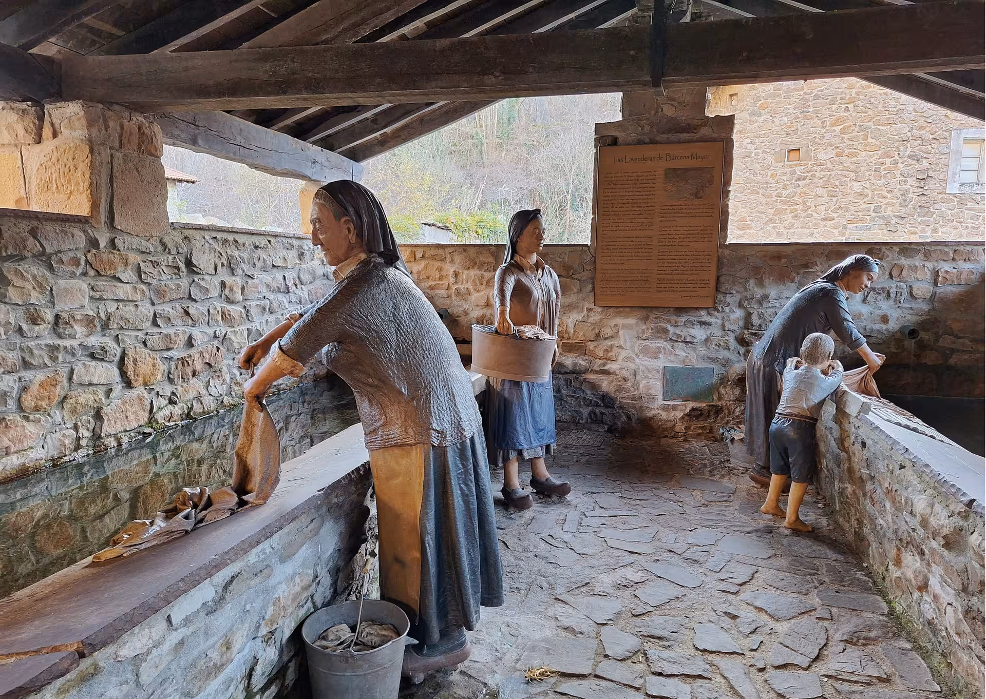 Traditional laundry washerwomen sculptures at historic stone wash house in Barcena Mayor Cantabria village tour