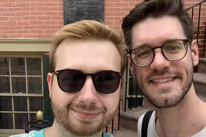 Two smiling men taking a selfie in front of a historic brick building with a bronze plaque in Washington DC