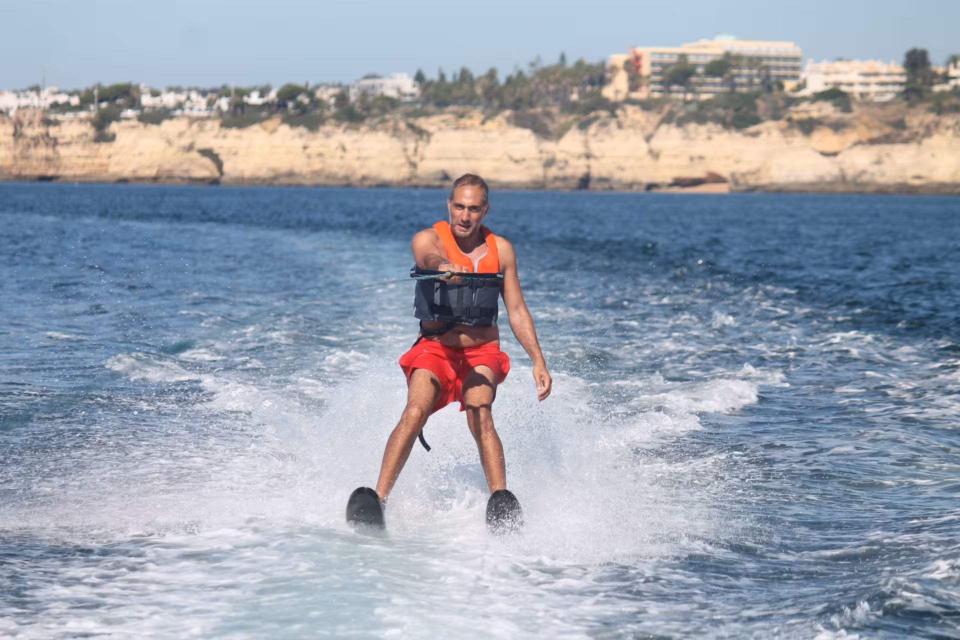 Man in orange life vest water skiing along the stunning coastline of Armacao de Pera Algarve Portugal