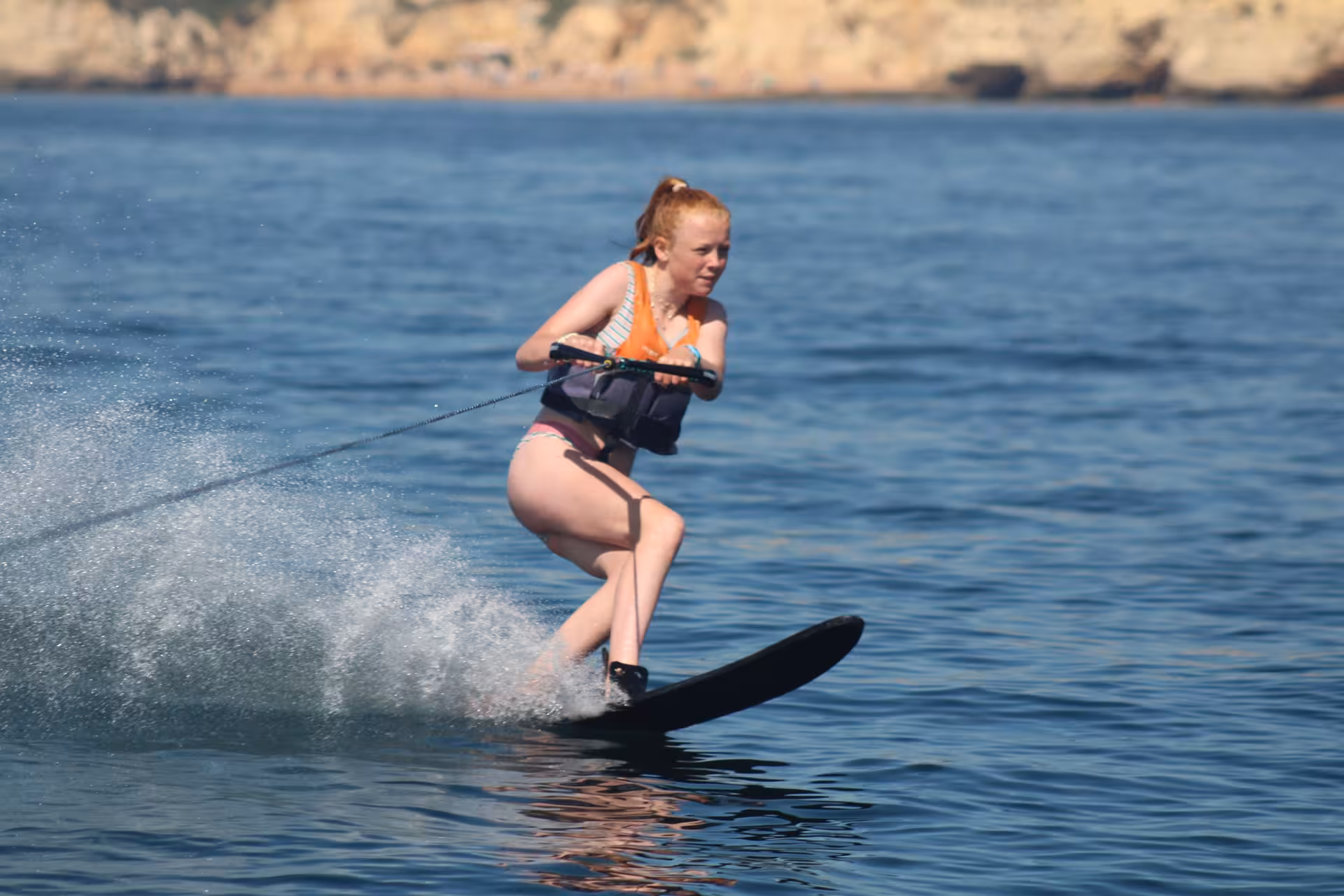 Young woman water skiing near scenic rocky cliffs of Armacao de Pera during a thrilling Algarve water ski tour