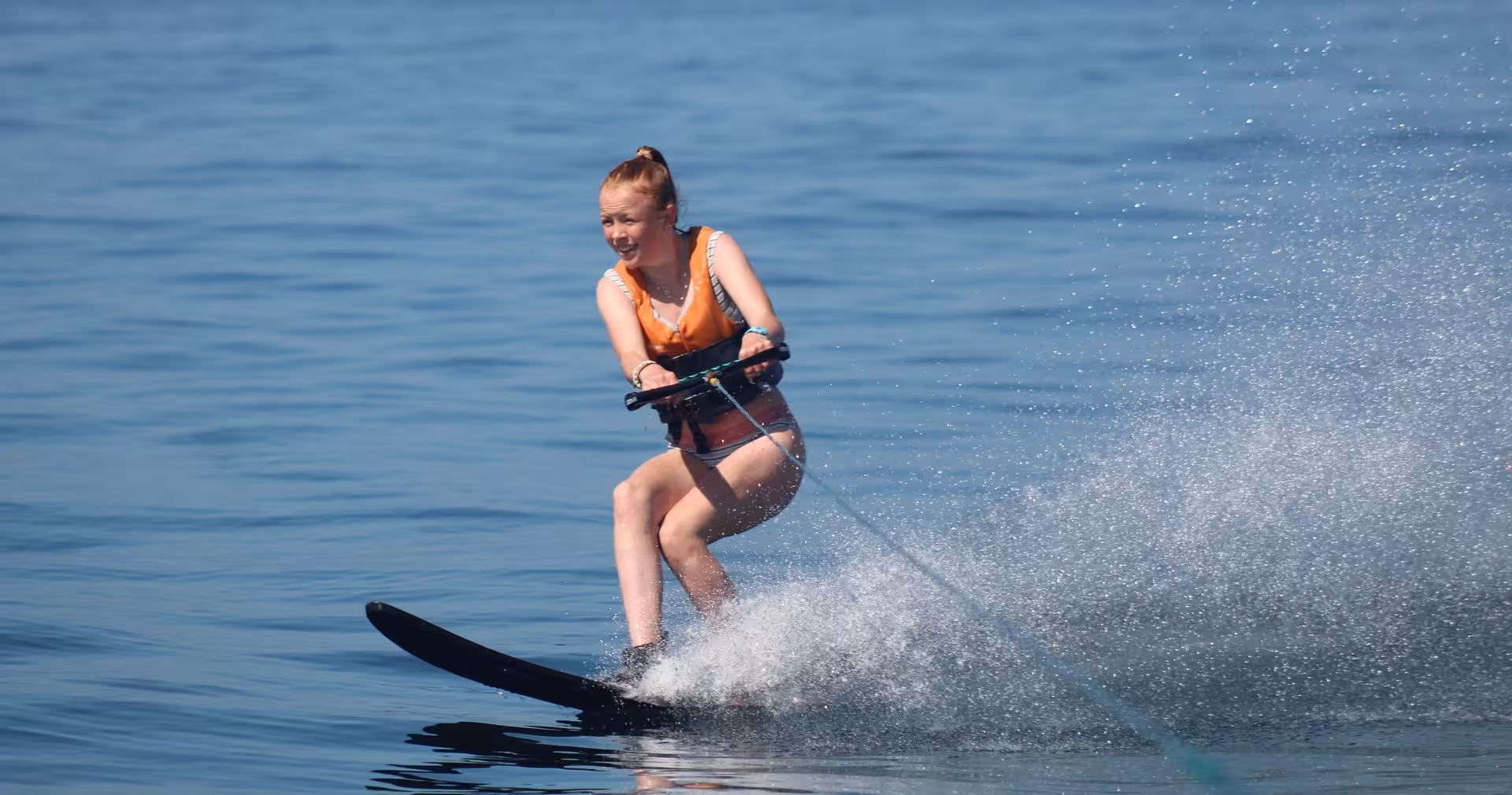 Young woman water skiing in Armacao de Pera Algarve wearing an orange life jacket on calm blue waters