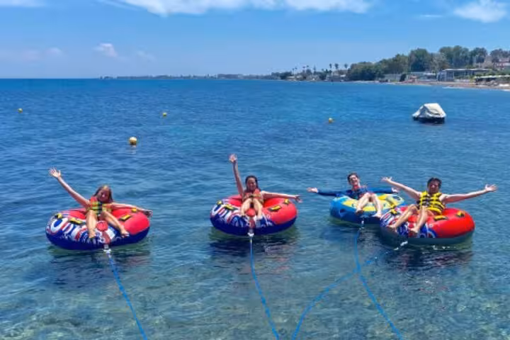 Four people on inflatable tubes waving on clear blue sea in Antibes French Riviera