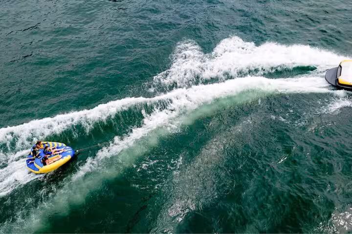 People riding a yellow and blue inflatable tube towed by a boat on turquoise waters in Antibes