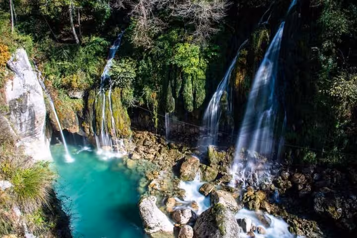 Scenic waterfall cascading into a turquoise pool surrounded by lush greenery on a private village tour.