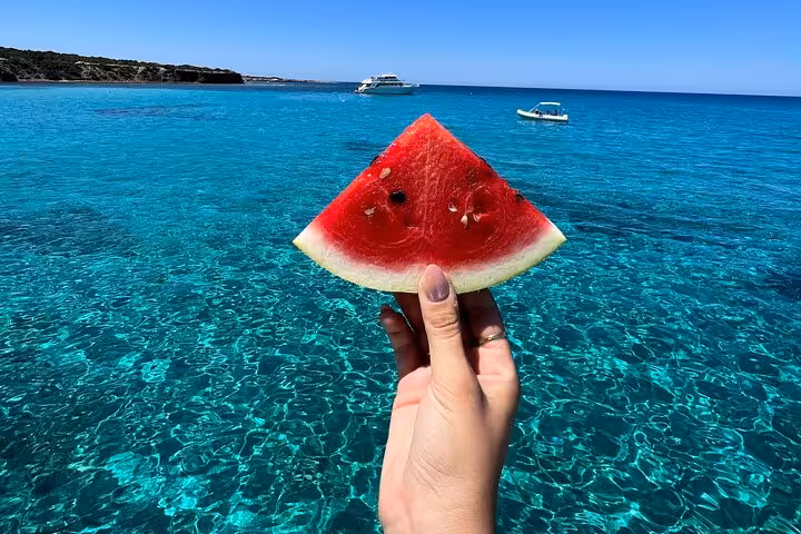 Watermelon snack on Blue Lagoon Akamas tour from Paphos, with glassy turquoise water and boats nearby