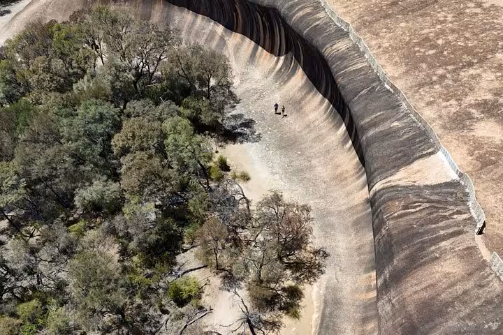 Aerial view of the iconic Wave Rock with visitors exploring its curved natural formation and surrounding trees.