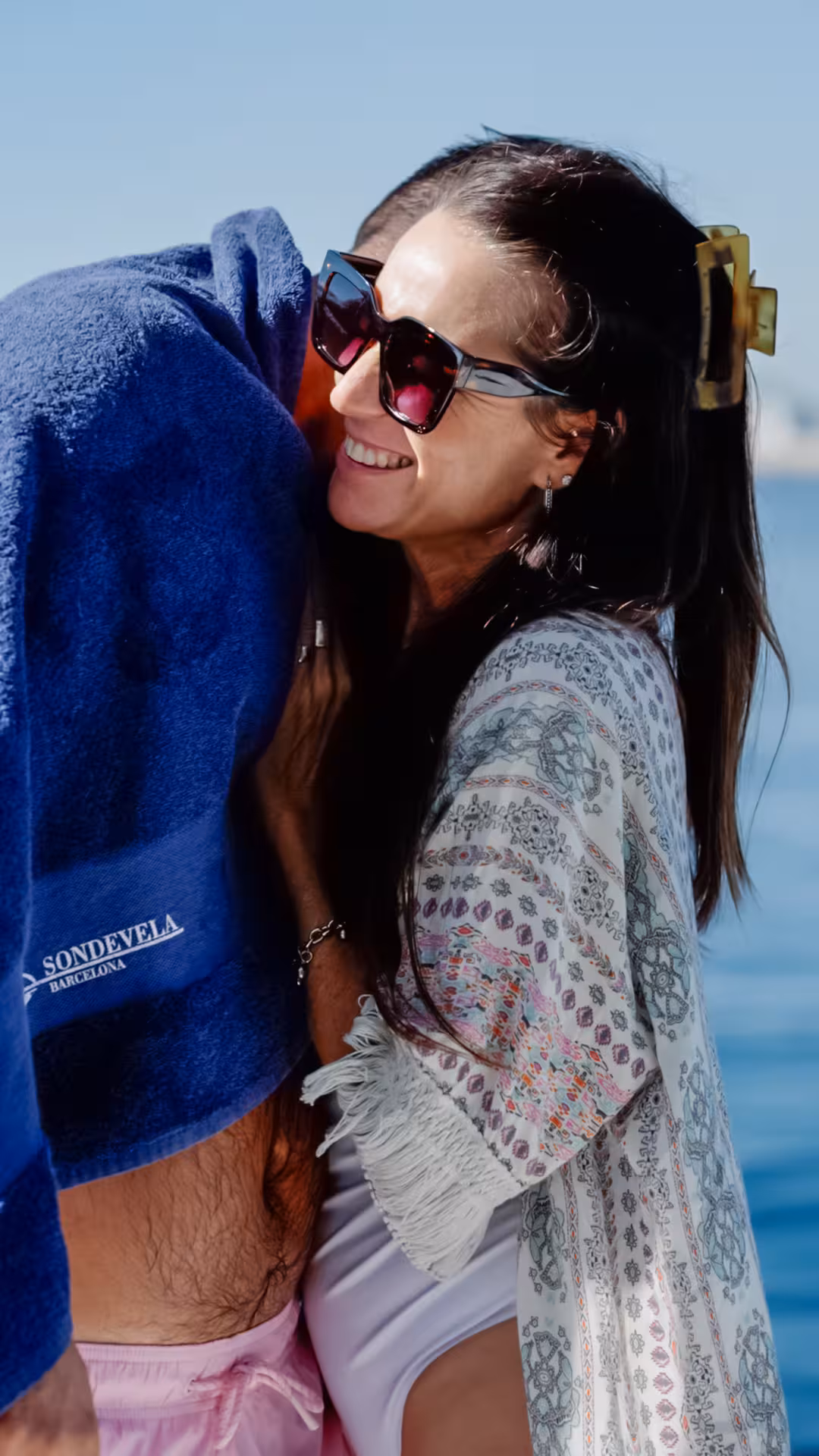 Smiling guest in sunglasses relaxes on a Barcelona wellness catamaran cruise, sea breeze and sunlit coast