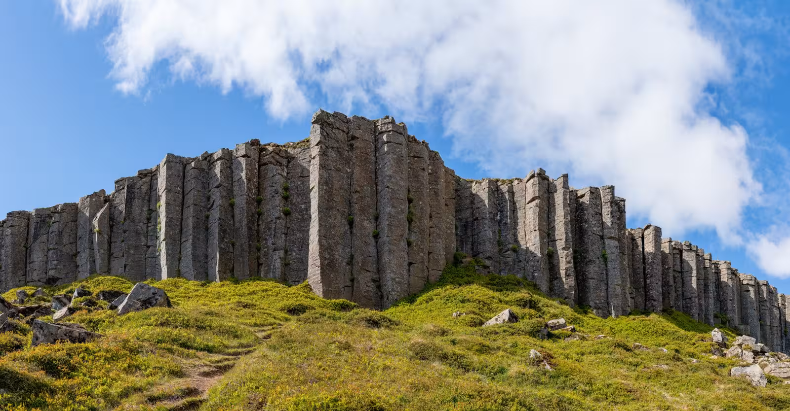 Dramatic basalt columns rise against a clear blue sky in West Iceland's picturesque landscape.