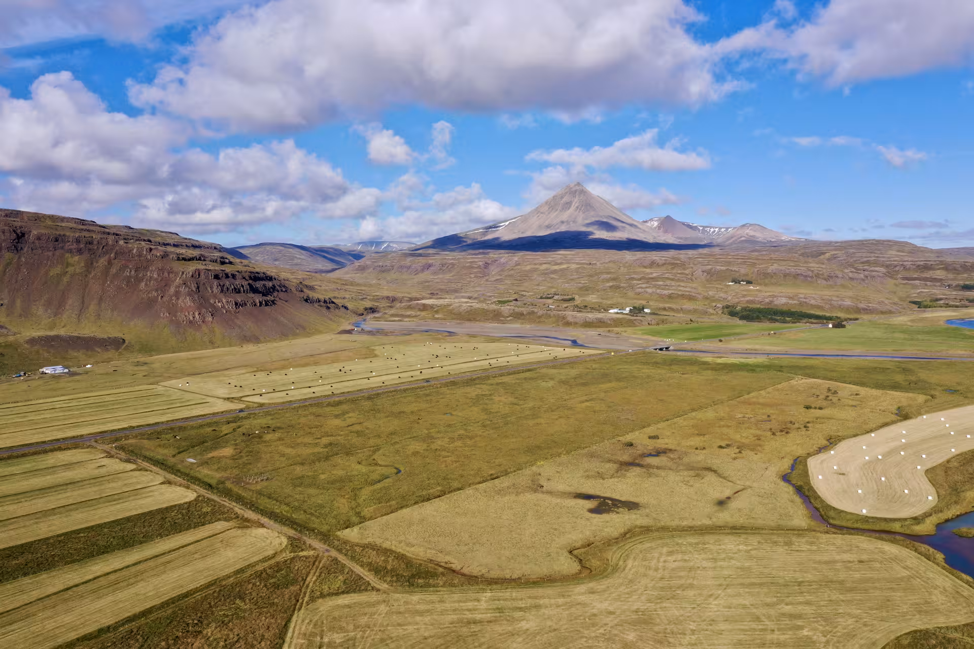 Aerial view of green farmlands and a volcanic mountain peak in West Iceland under a blue sky
