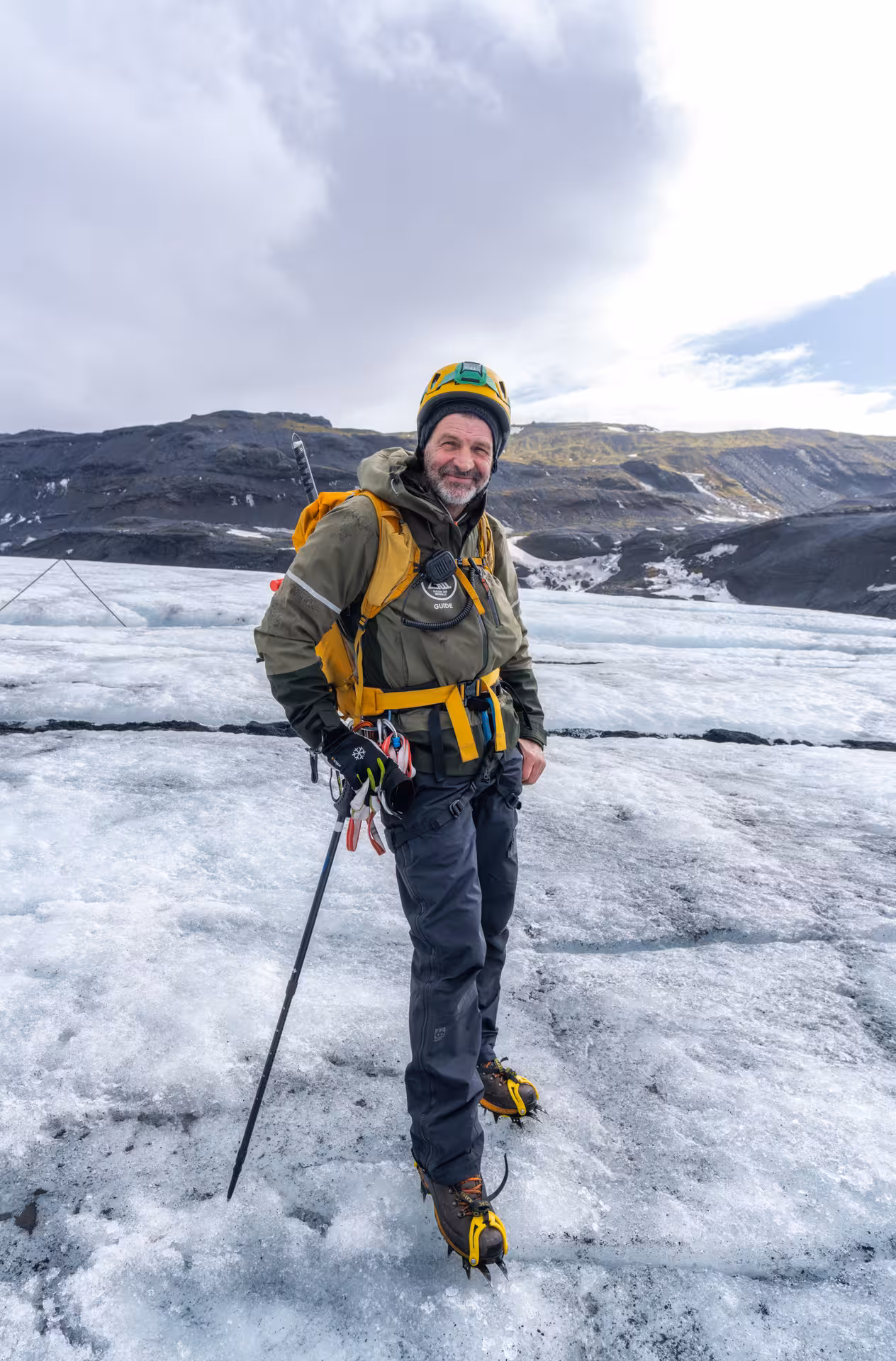 Glacier guide in yellow helmet and crampons standing on ice field in West Iceland