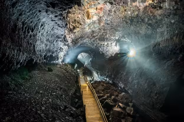 Illuminated lava tube cave with wooden walkway and dramatic light rays in West Iceland