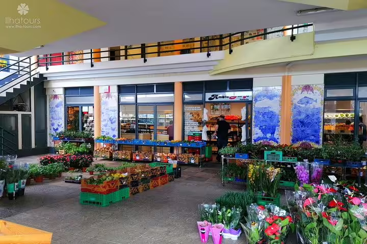 Colorful flower and produce market with an array of fresh plants and goods displayed under a covered walkway.