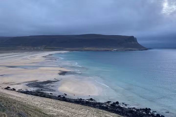 Turquoise waters and white sand beach with dramatic flat-topped cliffs in the Westfjords, Iceland