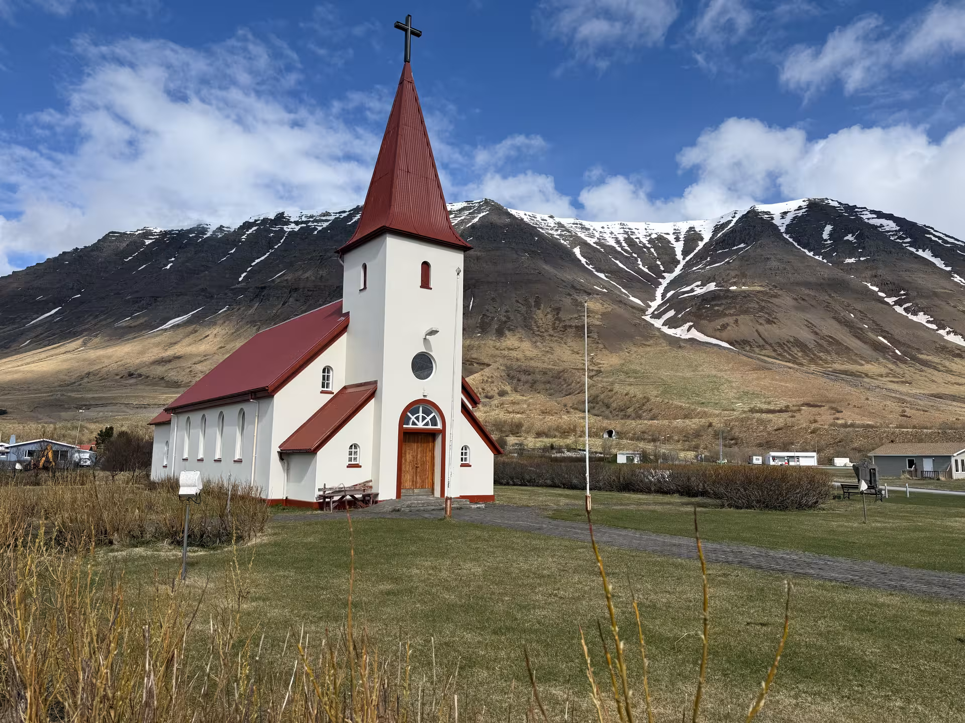 White church with red steeple and cross set against snow-capped mountains in the Westfjords, Iceland