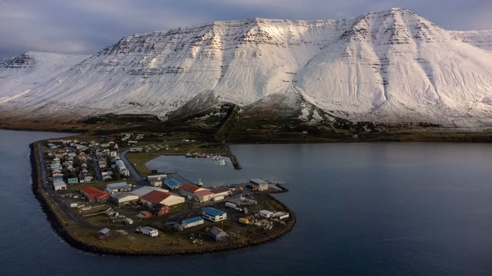 Aerial view of small coastal village on peninsula with snow-covered Westfjords mountains behind