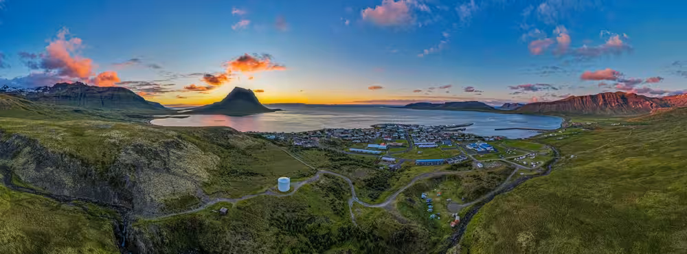 Aerial panoramic view of Westfjords Iceland coastal town nestled between green mountains and fjord at sunset