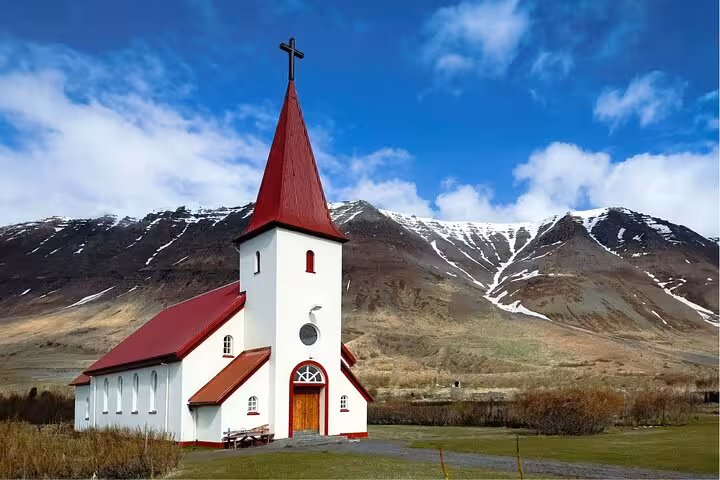 White church with red roof and steeple against snow-capped mountains in Westfjords, Iceland