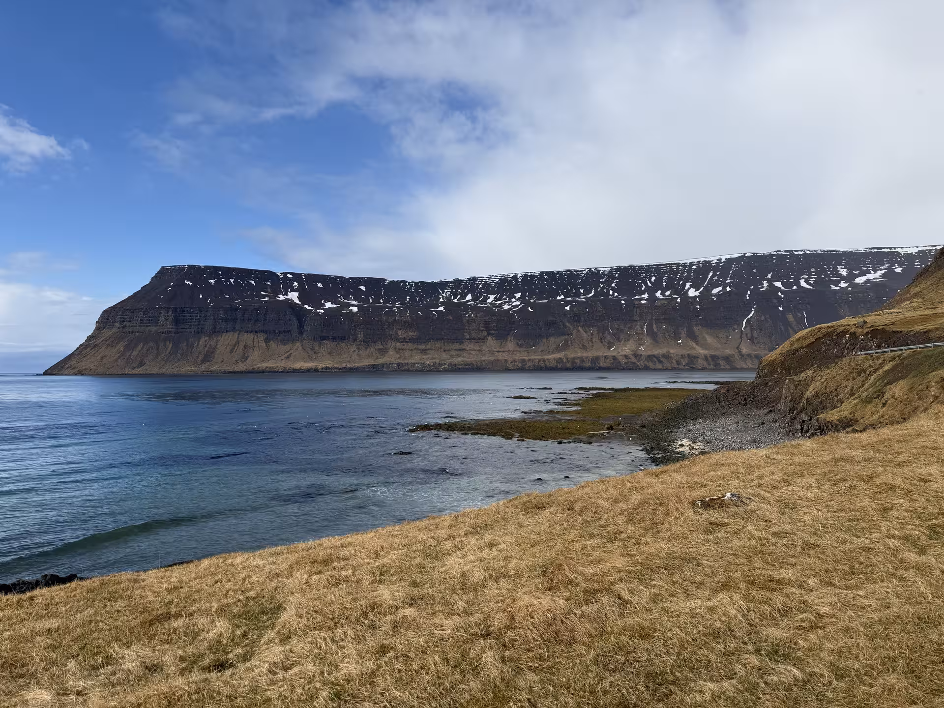 Snow-dusted flat-topped cliffs overlooking a calm fjord with golden grass foreground in the Westfjords, Iceland