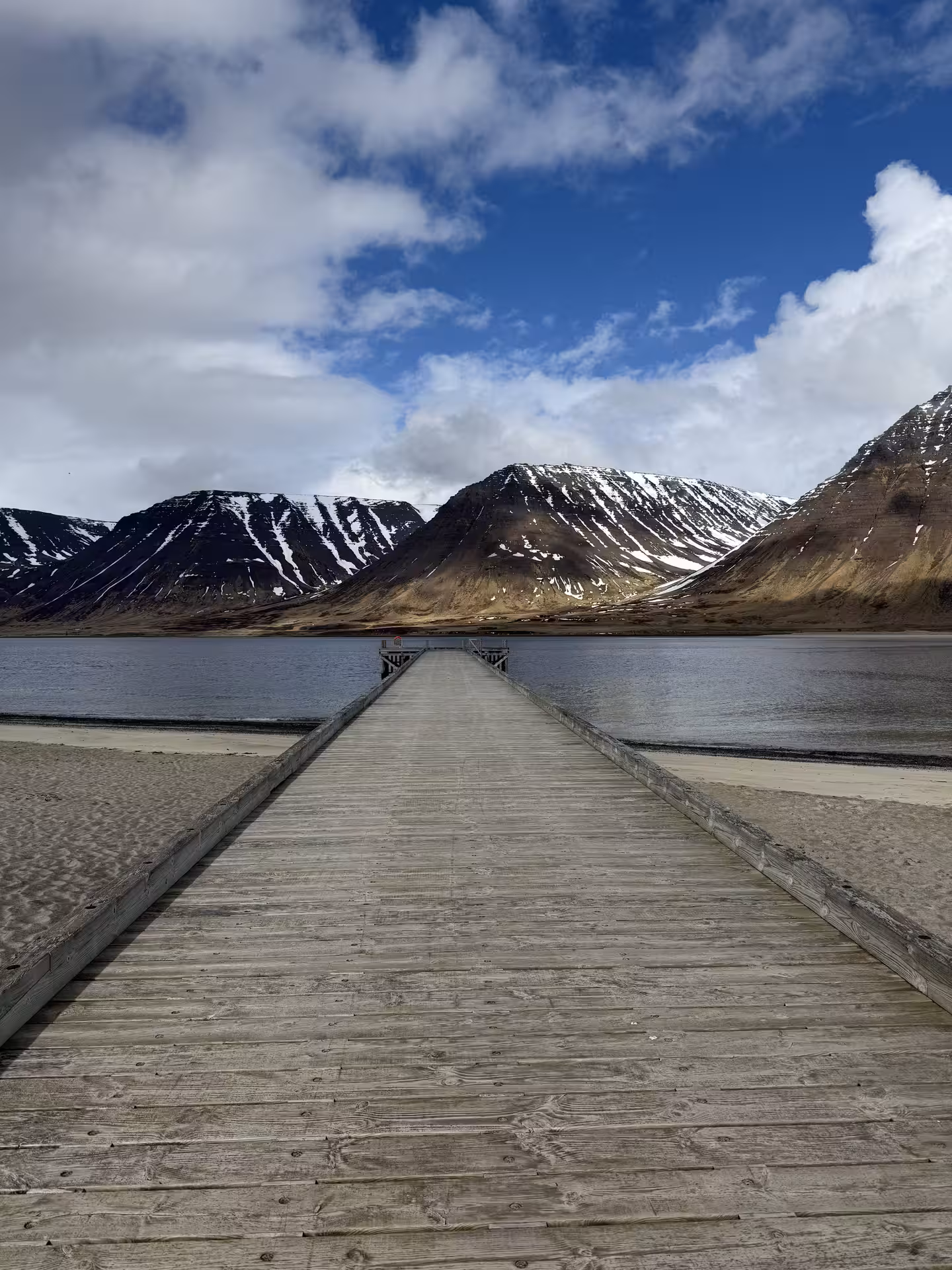 Wooden pier extending into a fjord with snow-streaked mountains in the Westfjords, Iceland