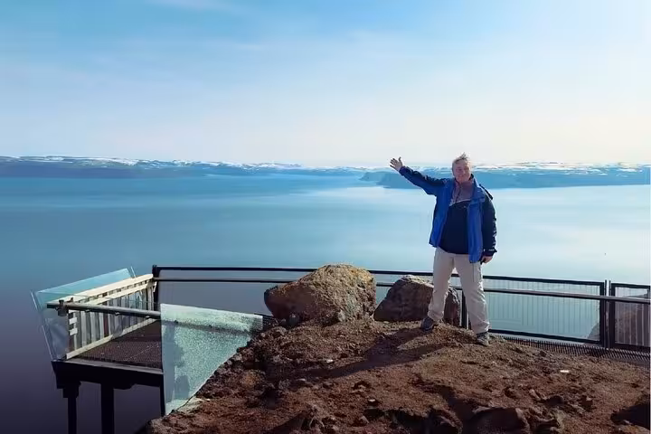 Tourist posing at scenic Westfjords overlook with vast fjord and snow-capped mountains in background, Isafjordur